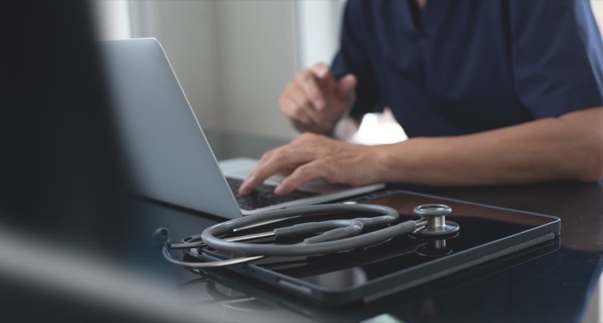 Doctor typing clinical documentation on a laptop in a medical office, representing AI scribe and EHR write-back workflows