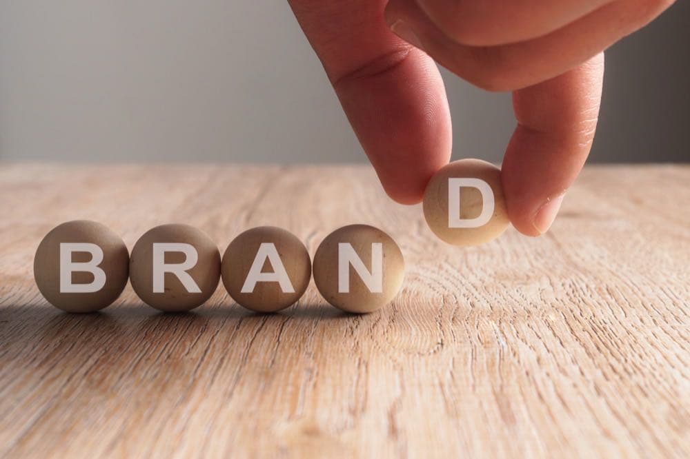 Hand placing a wooden block spelling BRAND, representing brand authority