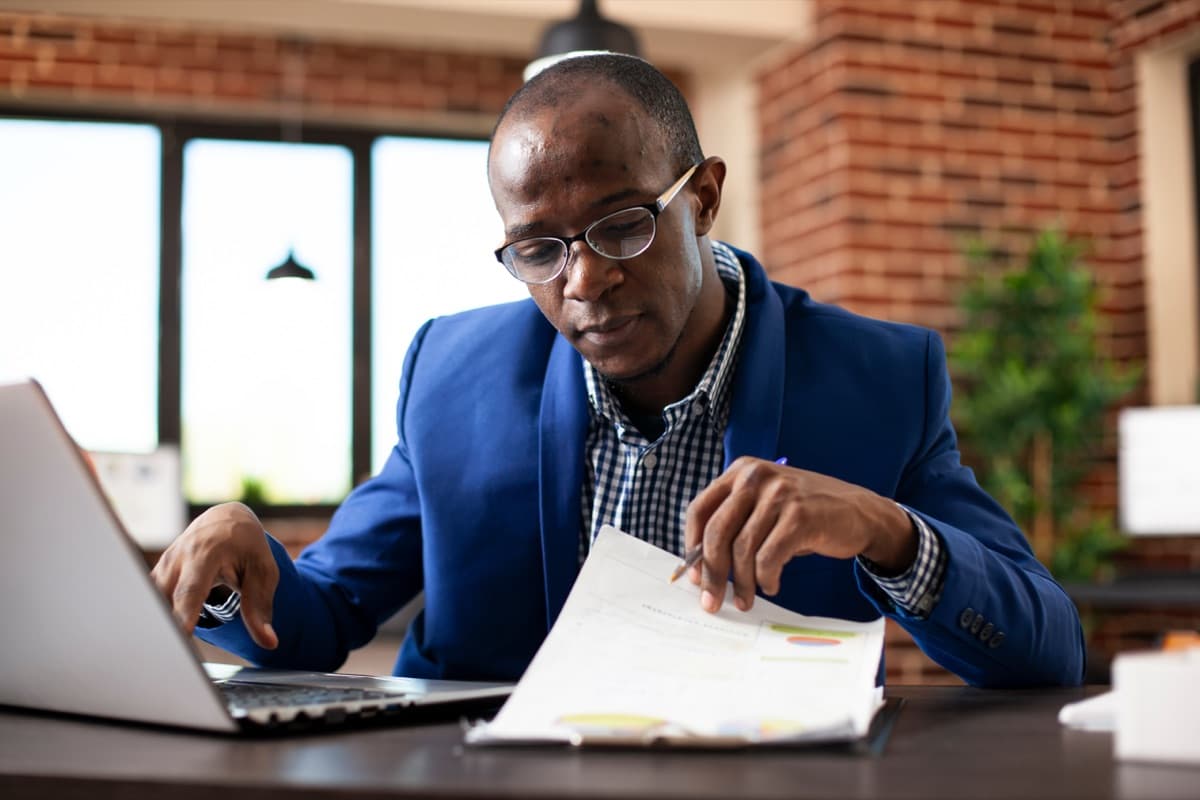 IT compliance analyst reviewing printed documents alongside a laptop during a workplace audit