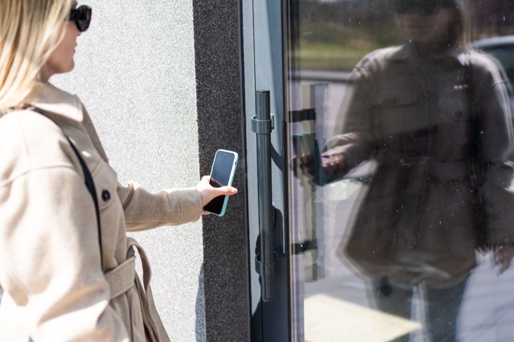 Person using a smartphone to tap into an electronic access reader, representing touchless mobile credentials