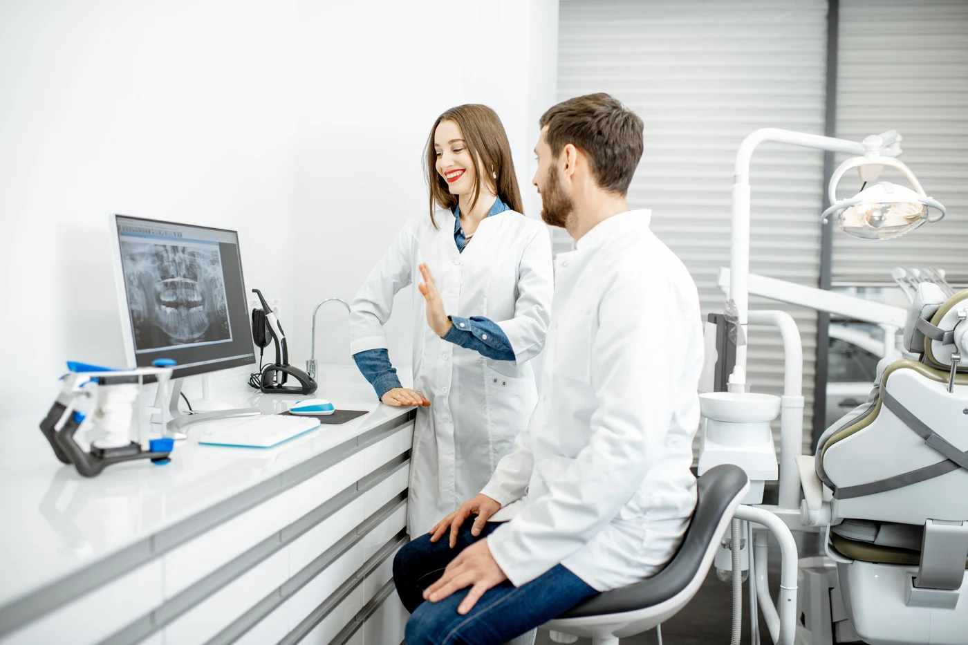 Two dental clinicians beside an operatory computer displaying a panoramic X-ray