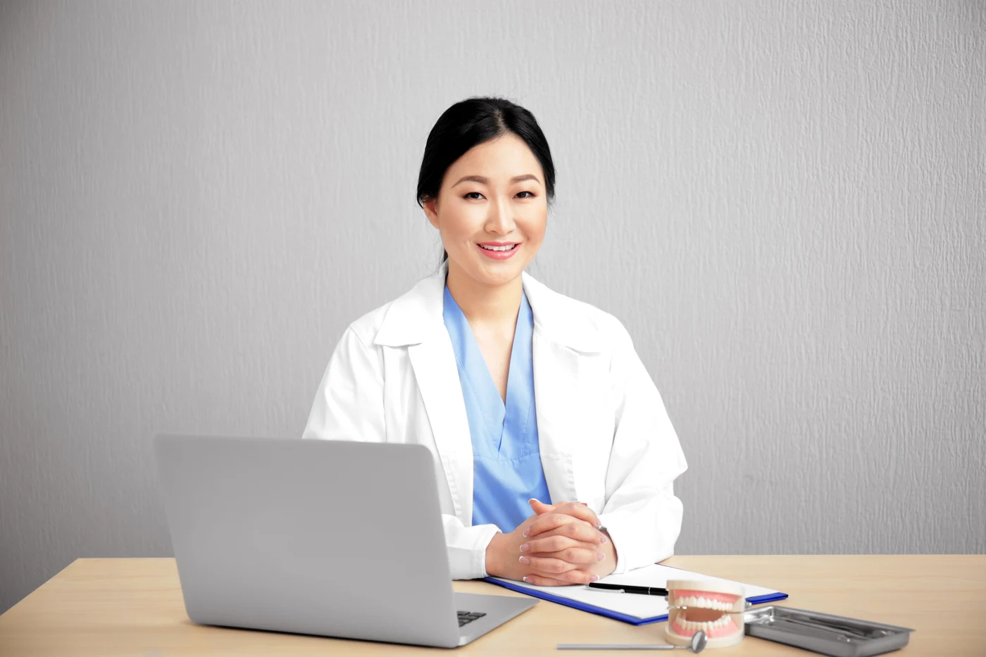 Dentist seated behind a laptop with a dental model and instruments on the desk