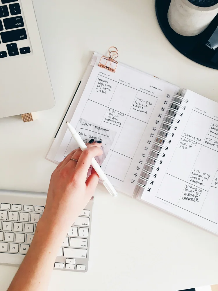 Overhead view of a planner, laptop keyboard and desk accessories