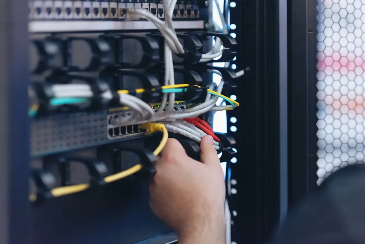Network technician connecting patch cables in a server cabinet where surveillance recorders and switches are racked