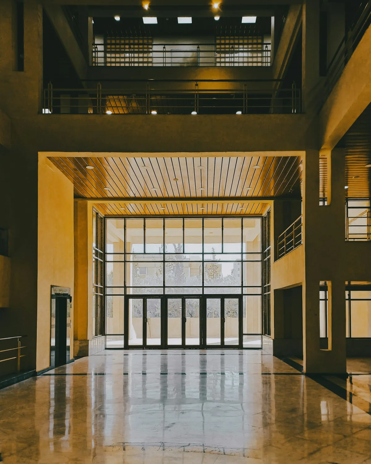 A tall lobby with reflective floors, glass entrance doors, and an upper-level balcony.