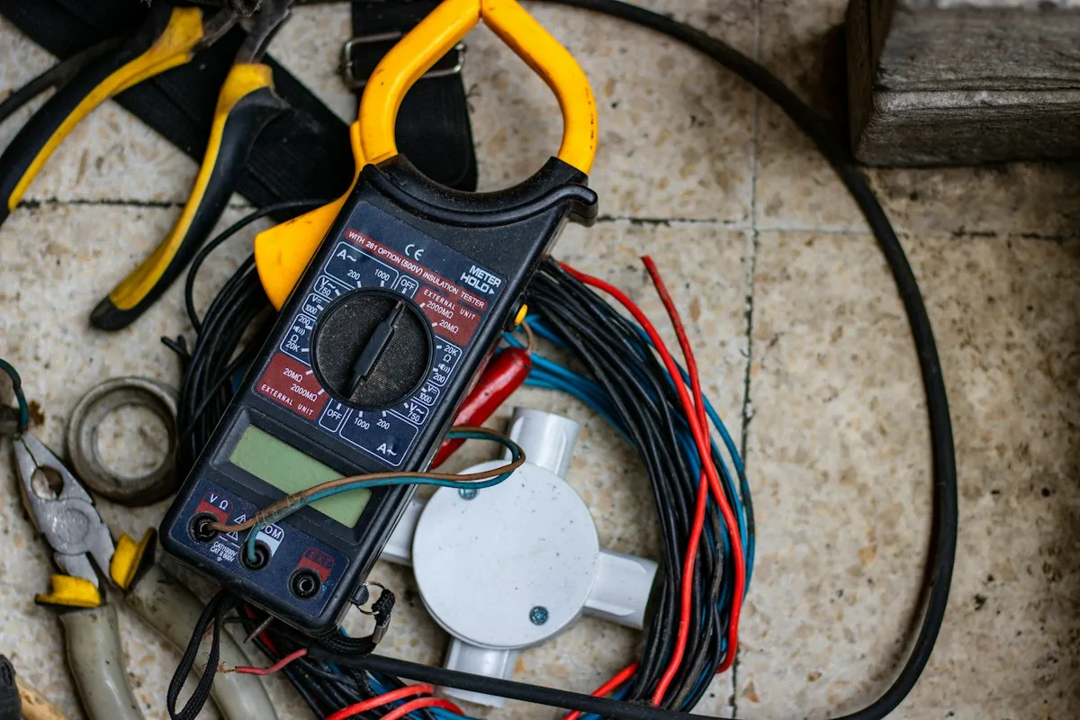 A handheld clamp meter with test leads beside electrical tools.