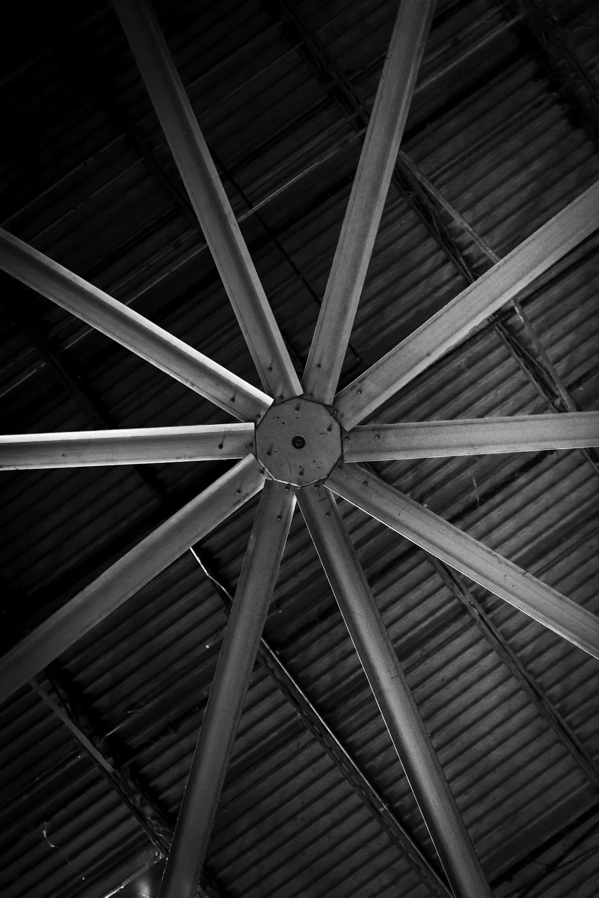Large ceiling fan beneath the exposed roof structure of a warehouse.
