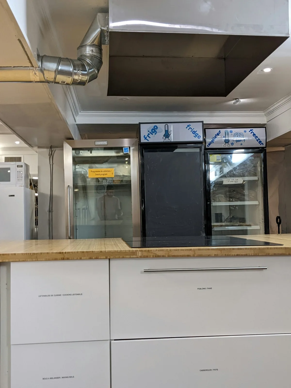 Commercial refrigerator and freezer cabinets behind a kitchen counter beneath an extraction hood.