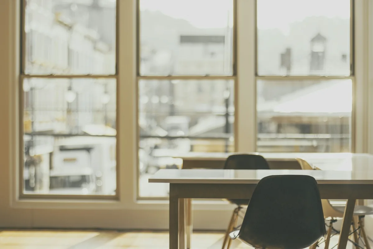 Office tables and chairs beside large framed windows.