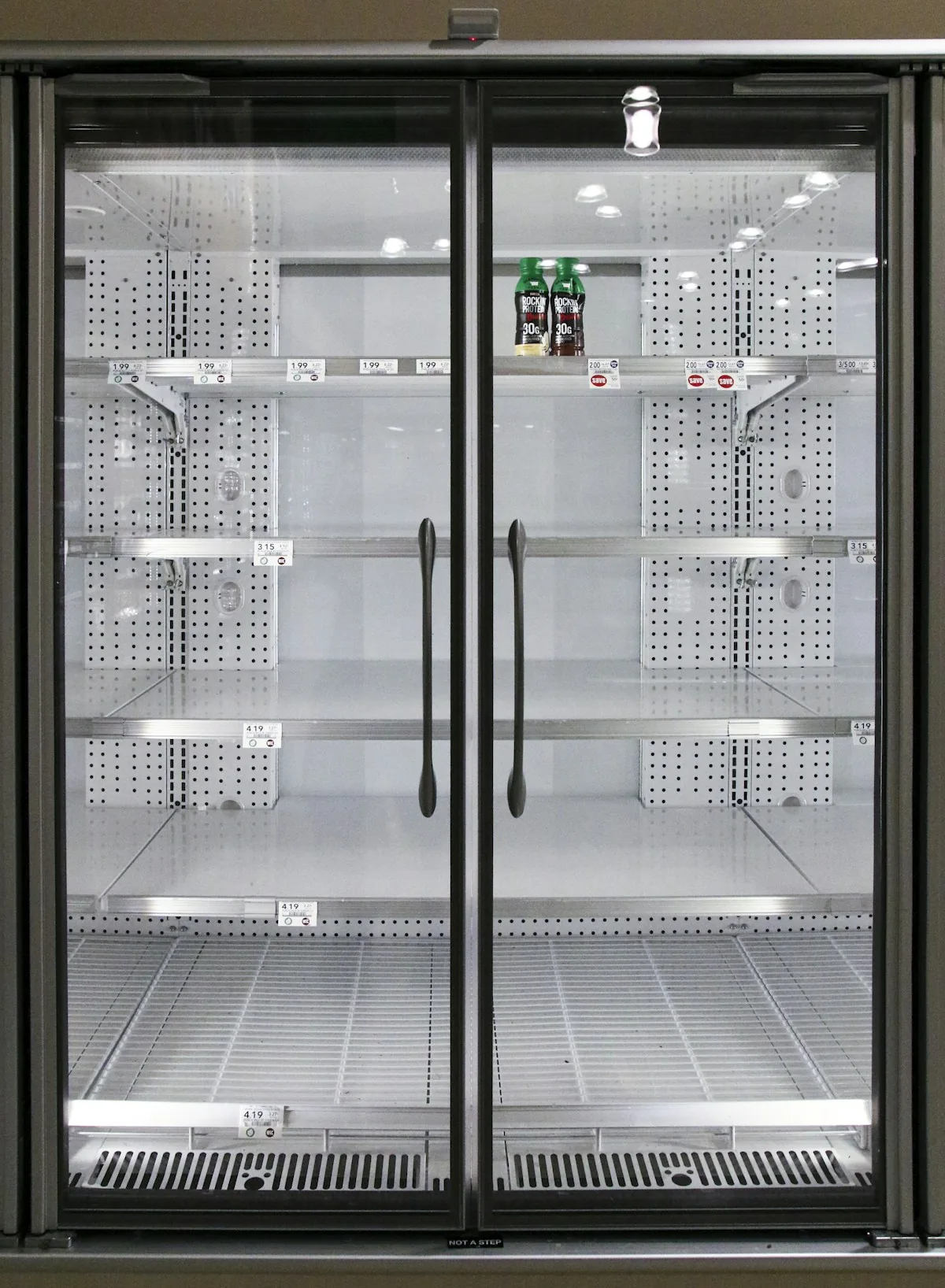A mostly empty commercial glass-door refrigerator with metal shelves.
