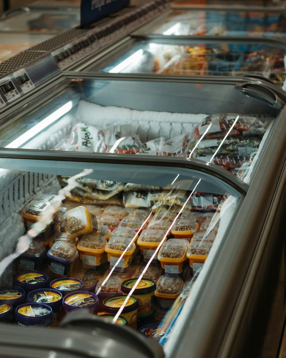 Packaged frozen foods arranged in glass-topped supermarket freezer cases.