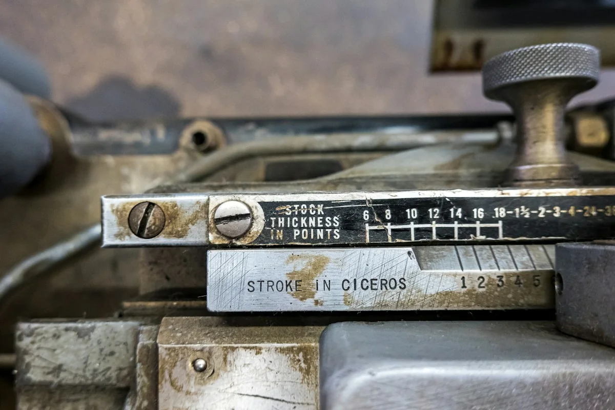 Engraved words and numbered scales on a metal typesetting-machine adjustment assembly.