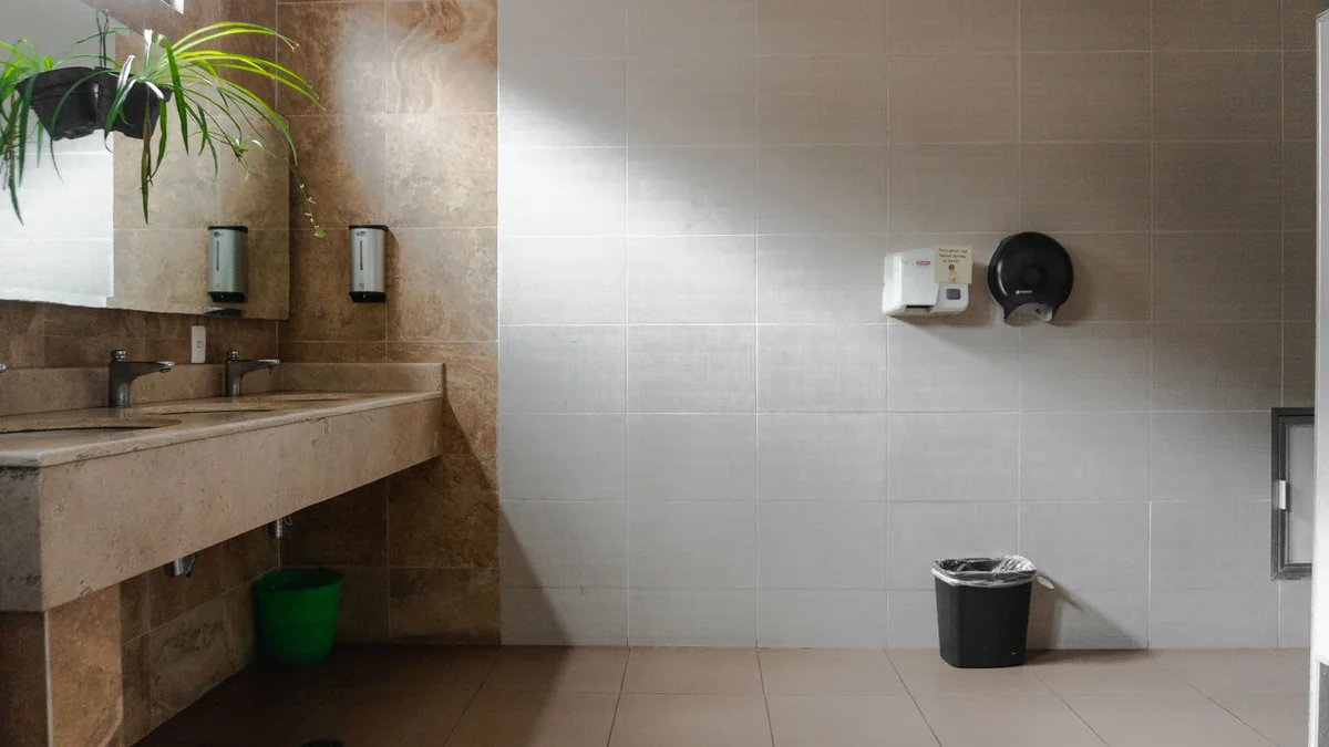 An empty restroom with a stone sink counter, wall-mounted dispensers and a mirror.