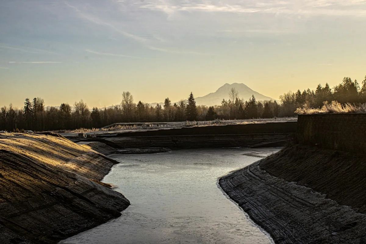 Water runs through an engineered open channel bordered by sloping banks.