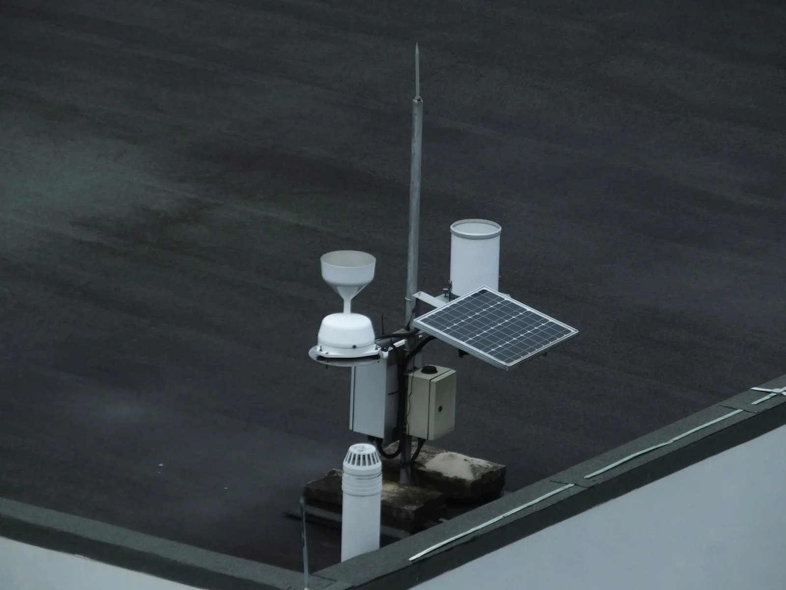 Compact weather instruments and a small solar panel mounted at a rooftop edge.
