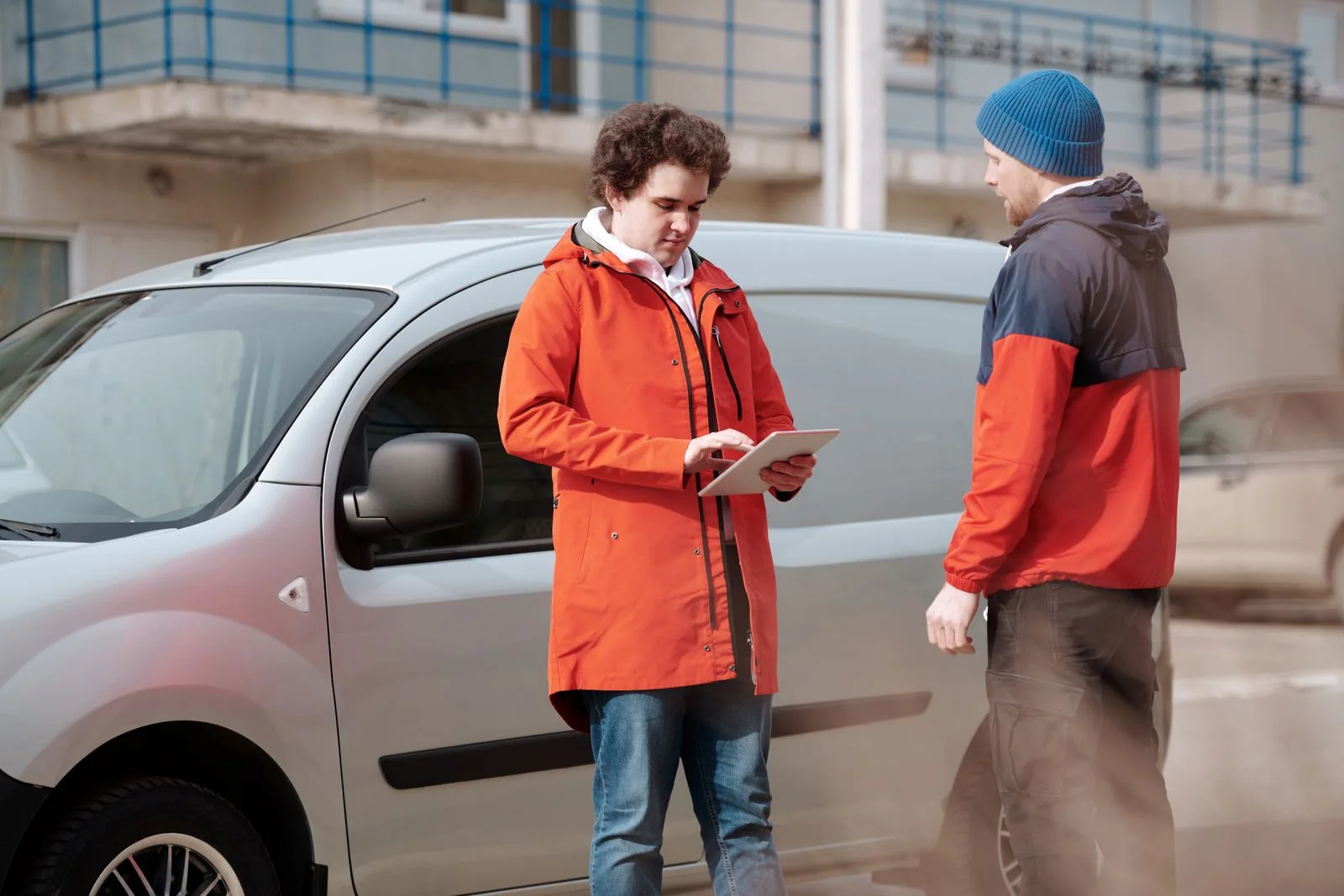 Two workers beside a silver work van reviewing a tablet.