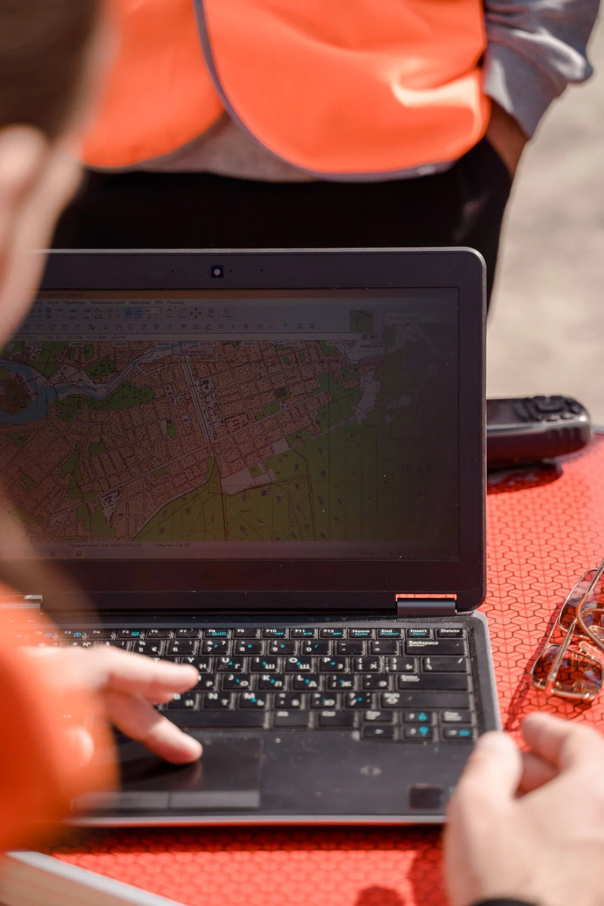 Hands using a laptop outdoors beside bright high-visibility workwear.