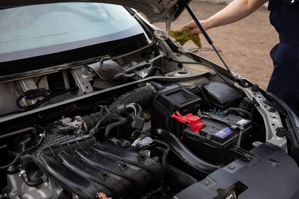 Open vehicle engine bay with a battery and red terminal cover at the right.