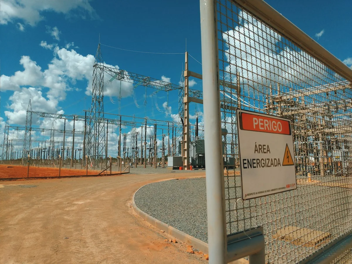 Electrical substation behind a metal gate with a high-voltage warning sign.