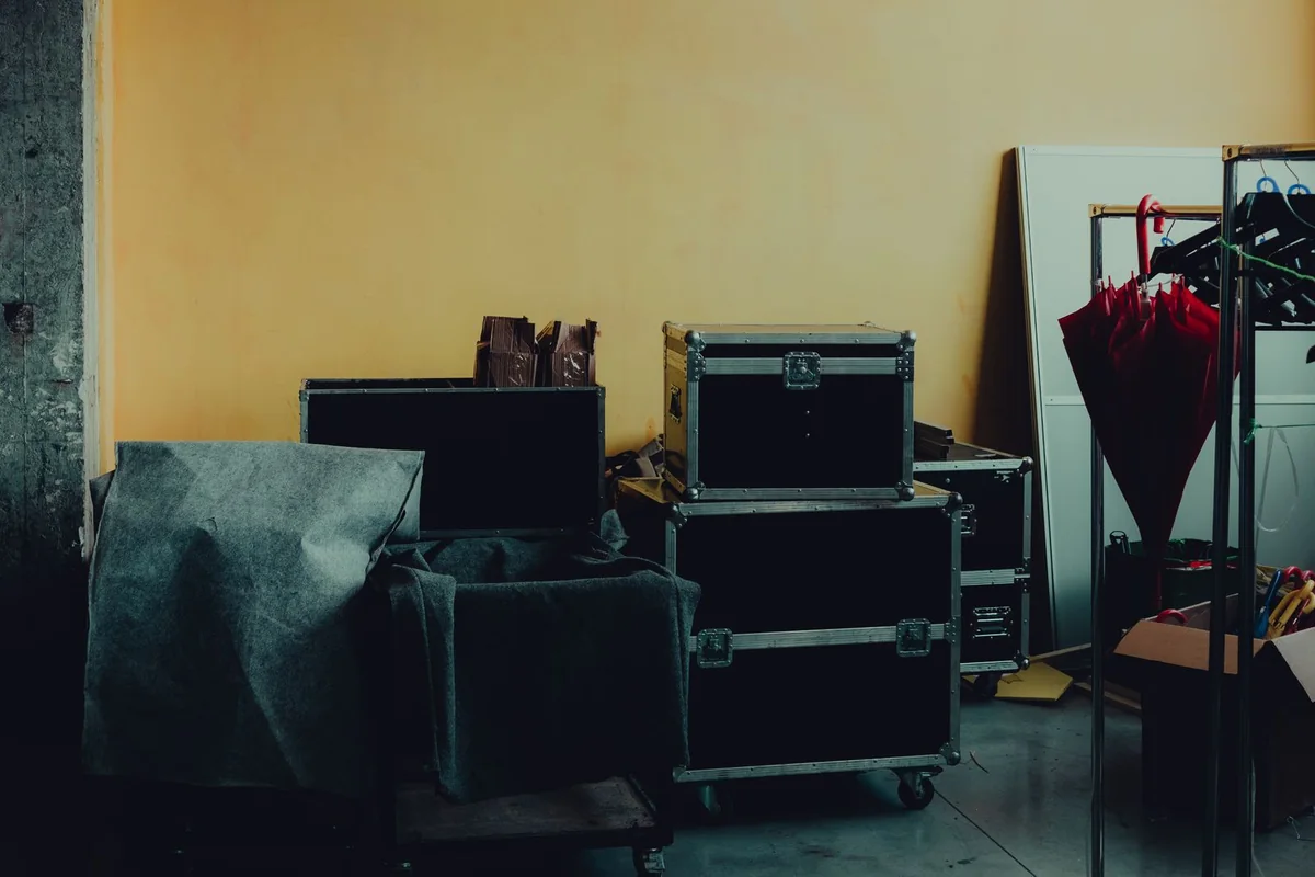 Wheeled equipment flight cases stored beside covered furniture and a garment rack.