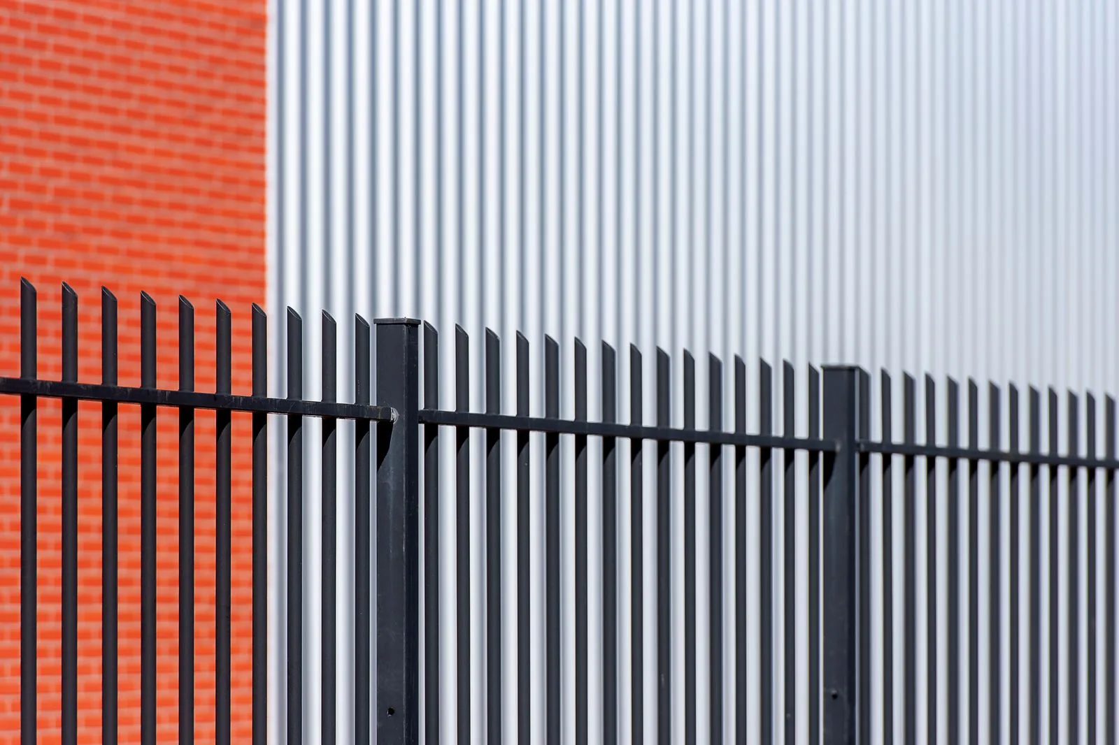 Black metal security fencing in front of a corrugated industrial building.