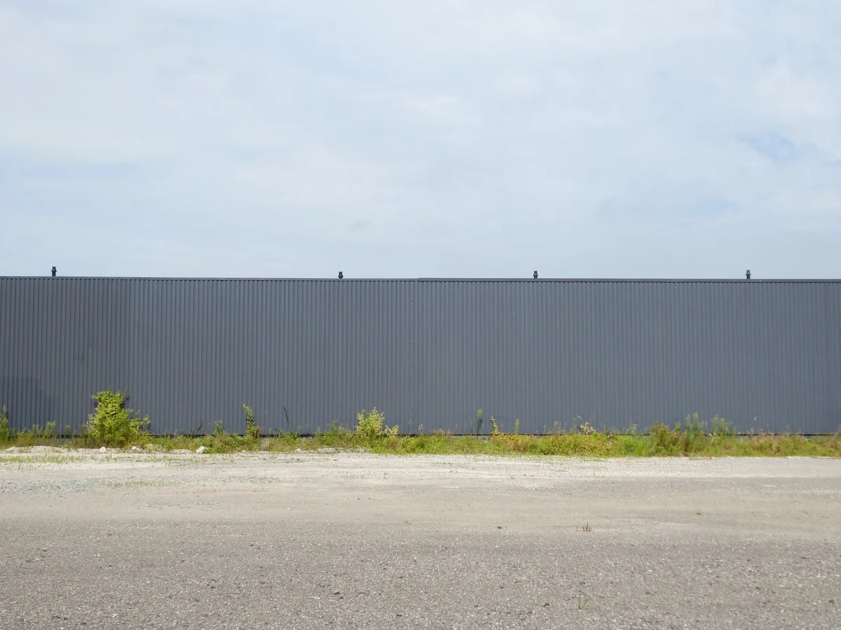 Long corrugated metal fence beside an open paved yard under a cloudy sky.