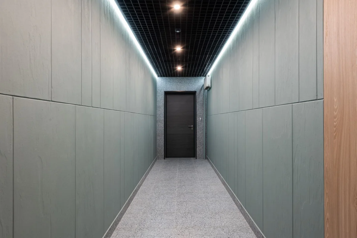 Empty modern corridor ending at a closed door beneath recessed ceiling lights.
