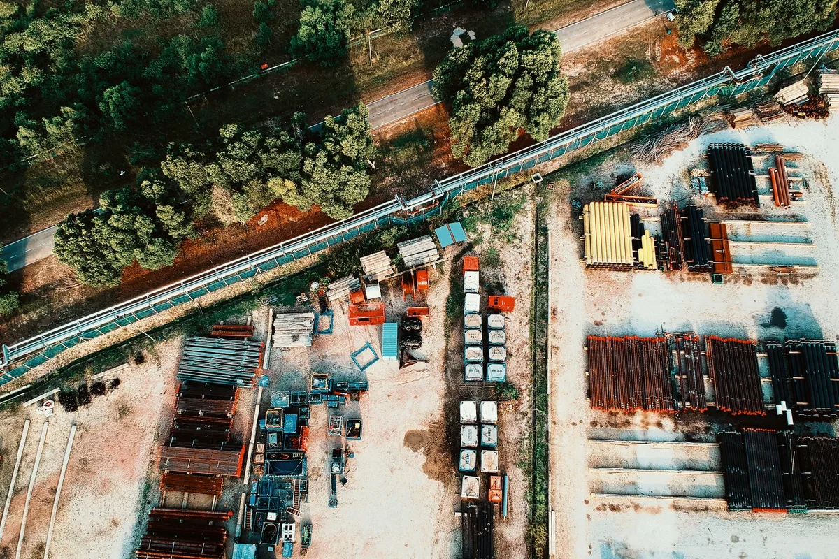 Aerial view of an outdoor industrial yard with stacked materials, access roads and bordering trees.