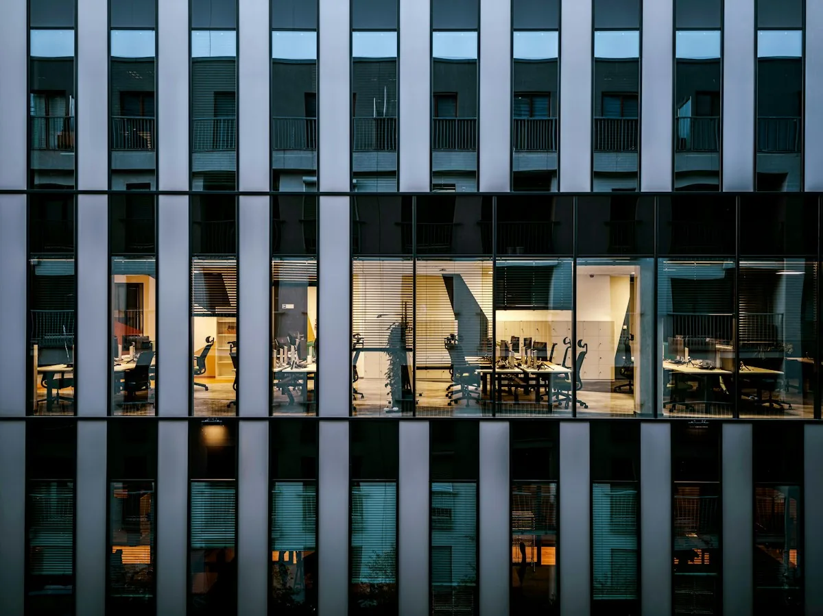 Office building facade with several illuminated rooms visible through tall windows.