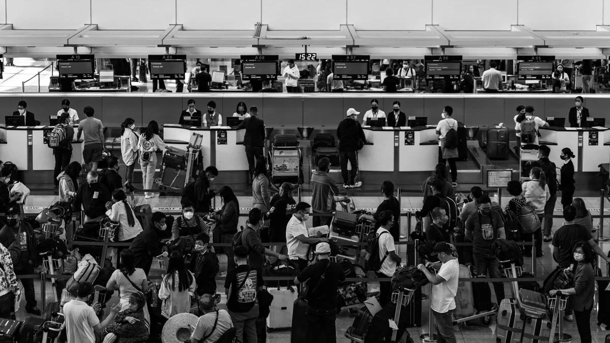Black-and-white view of passengers waiting in front of airport check-in counters.