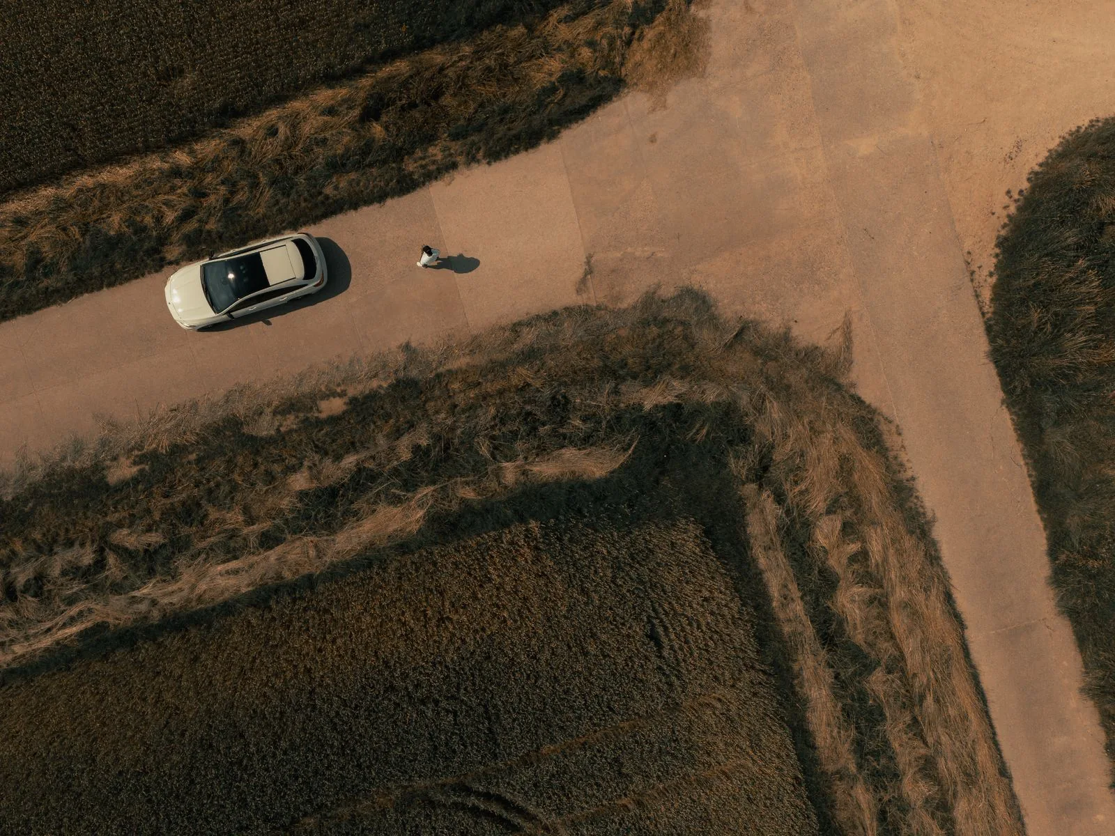 Overhead view of a car on an unpaved rural access road between fields.