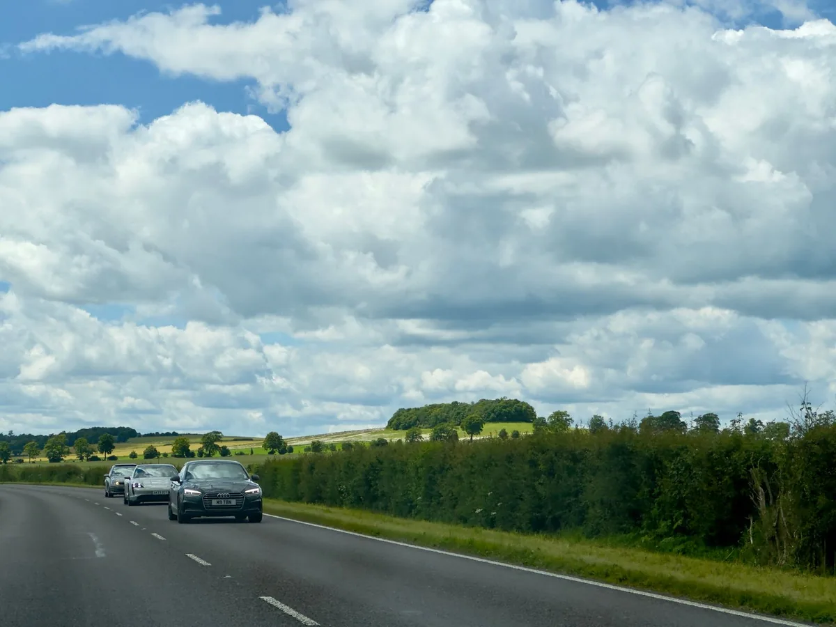 Cars approaching along a two-lane country road bordered by a green hedge.