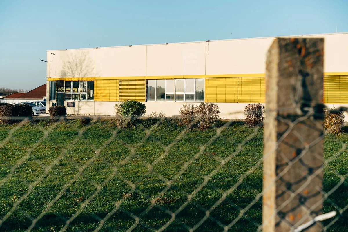 Industrial building and parked vehicles behind a chain-link boundary fence.