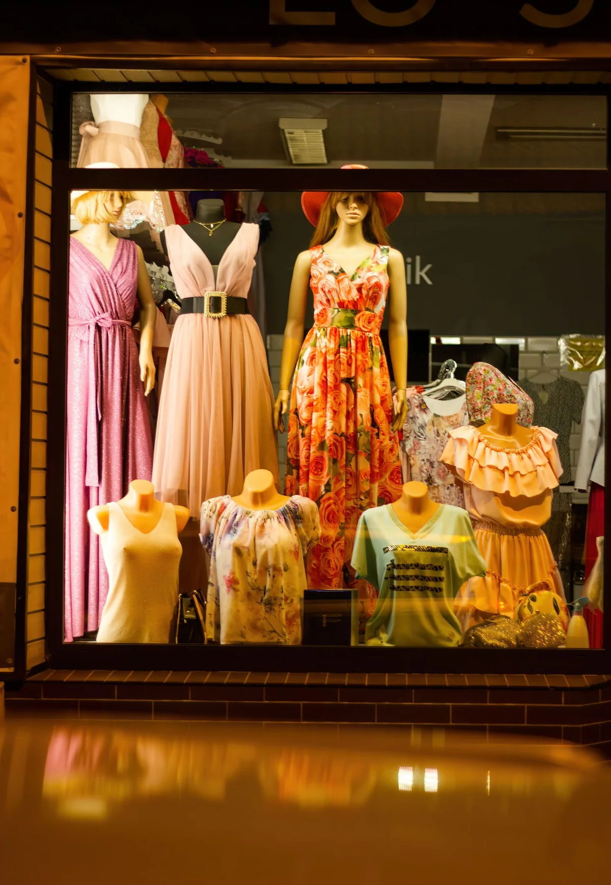 A warmly lit shop window displaying dresses on mannequins.