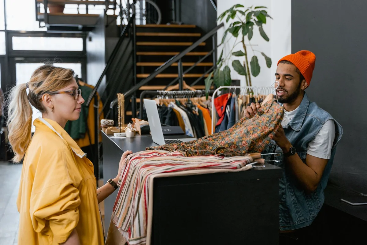 A shopper speaking with a member of staff at a clothing-store counter.