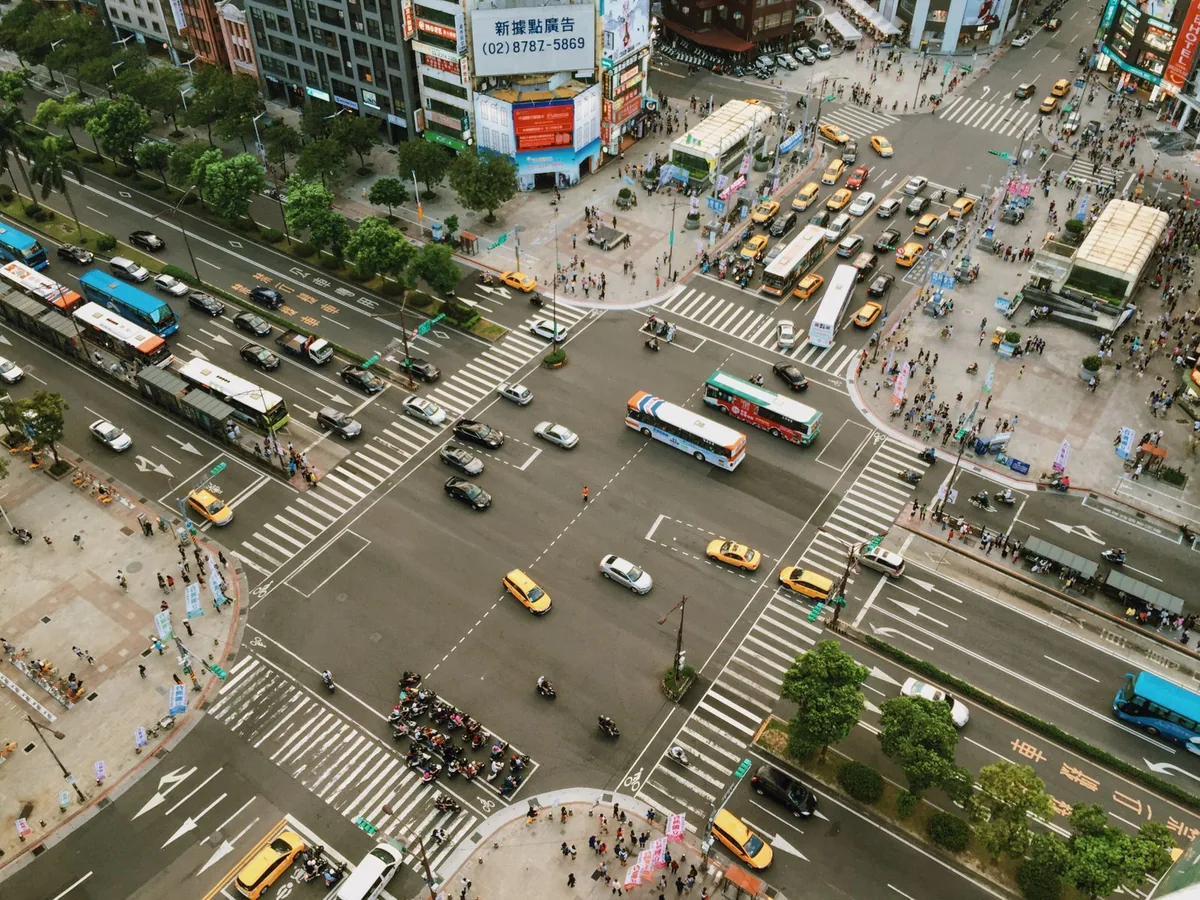 High-angle view of vehicles, marked lanes and pedestrian crossings at a city intersection.