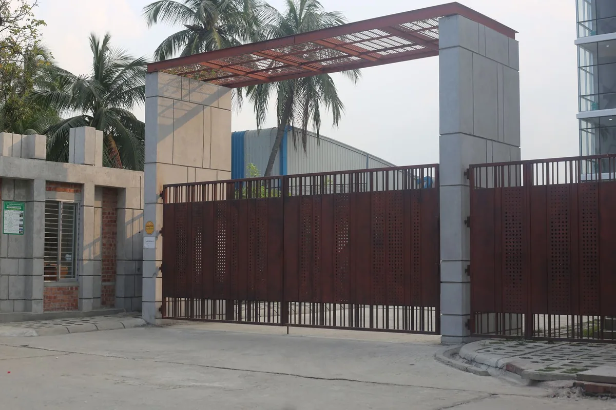 Wide metal entrance gate and paved vehicle approach beside a modern commercial building.