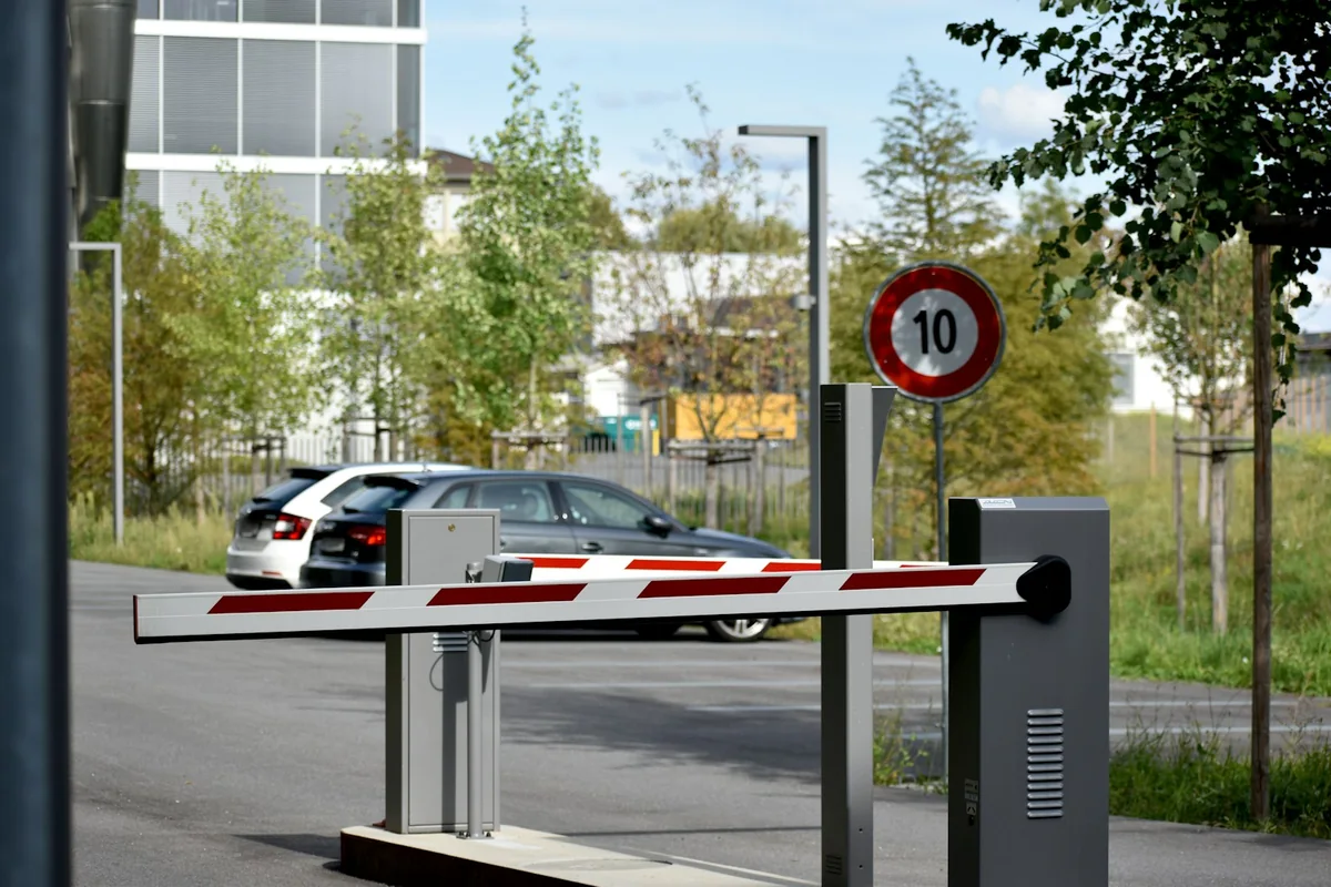Car behind red-and-white access barriers beside a modern building and a speed-limit sign.