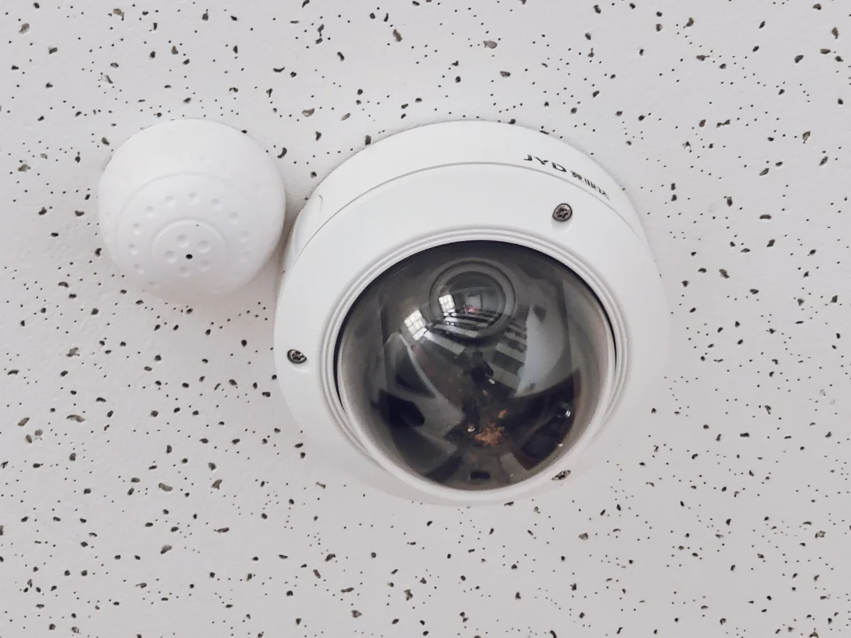 Dome surveillance camera mounted in a speckled suspended ceiling.