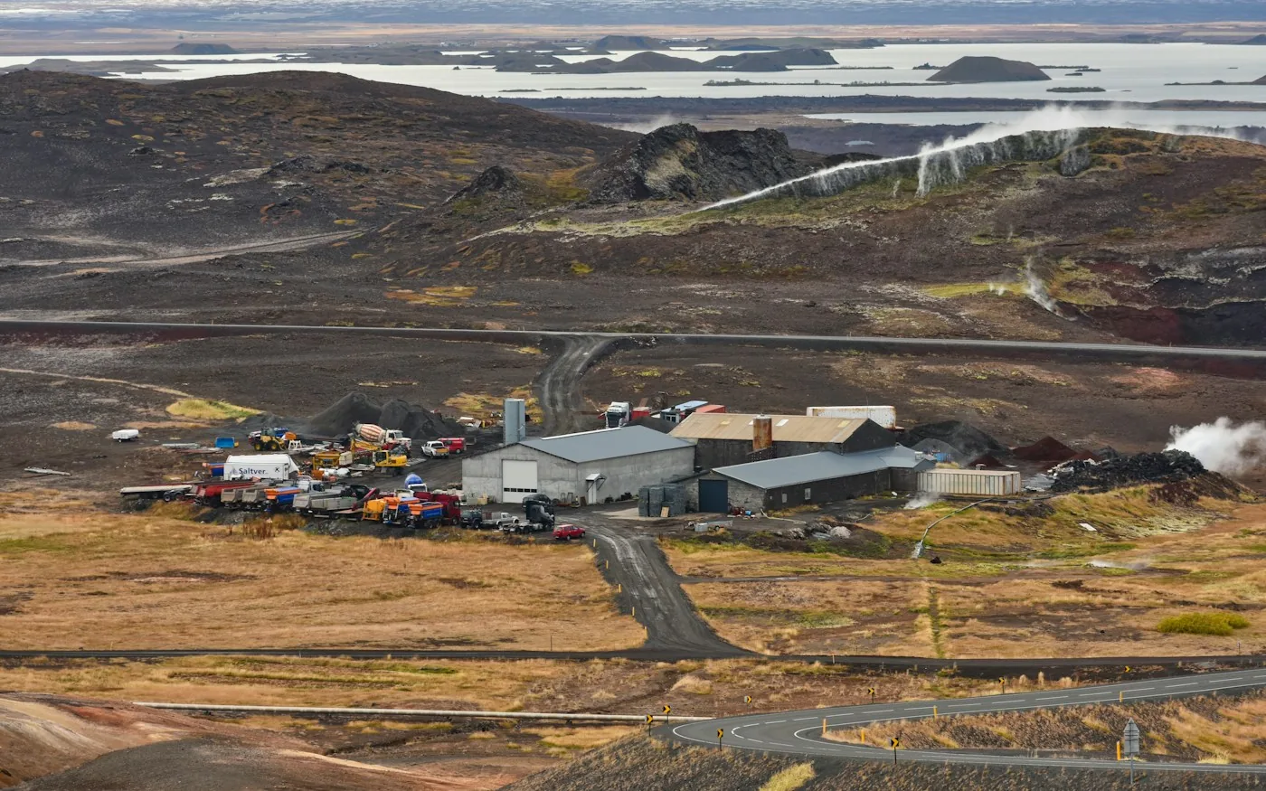 Industrial buildings and work vehicles in a remote rocky landscape.