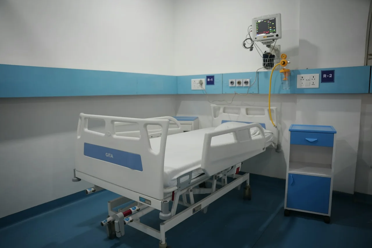 An empty adjustable hospital bed with raised side rails and a bedside cabinet.