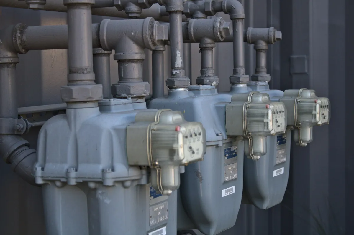 A row of gas utility meters and connected pipework outside a building.