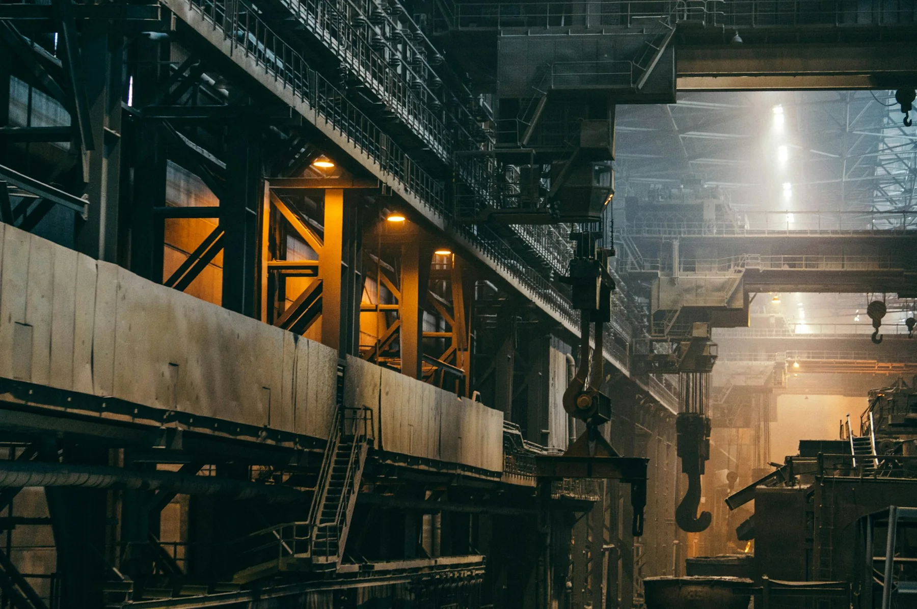 Wide industrial hall with steel structure, overhead equipment and production machinery.