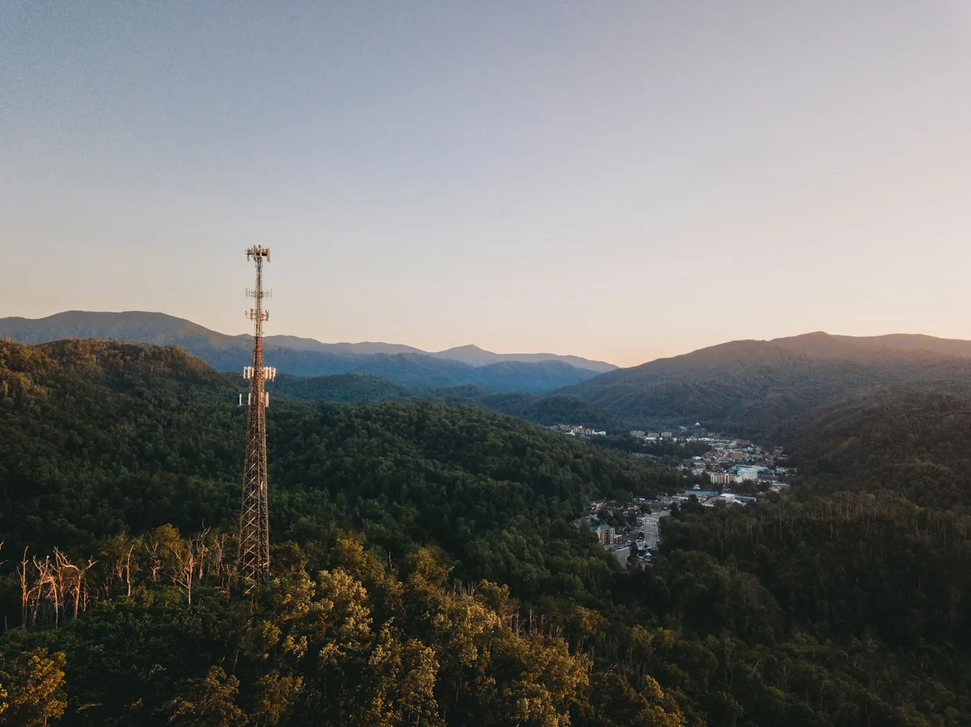 Telecommunications tower overlooking buildings in a wooded valley.