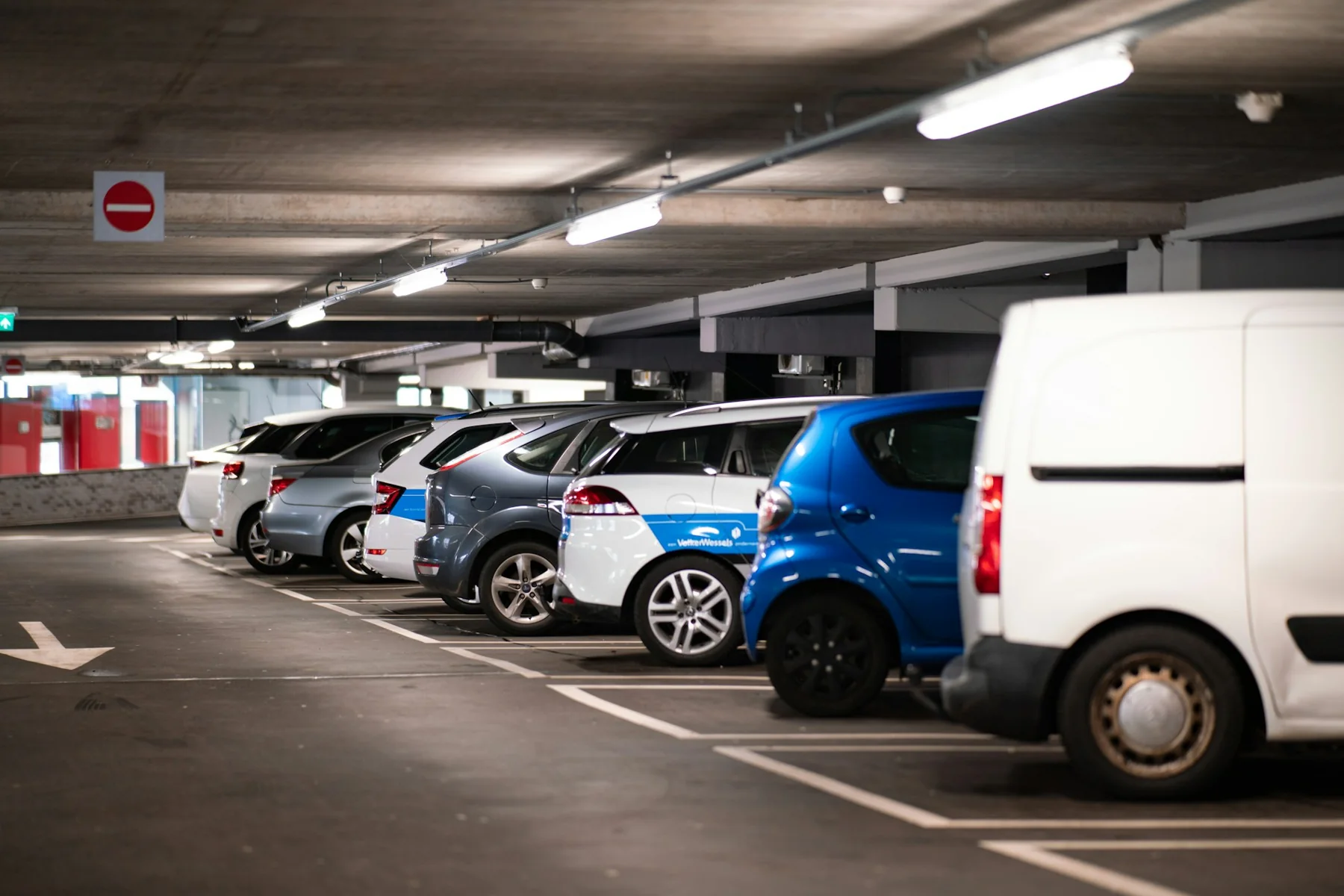 Cars and a van parked in marked bays inside a concrete parking garage.