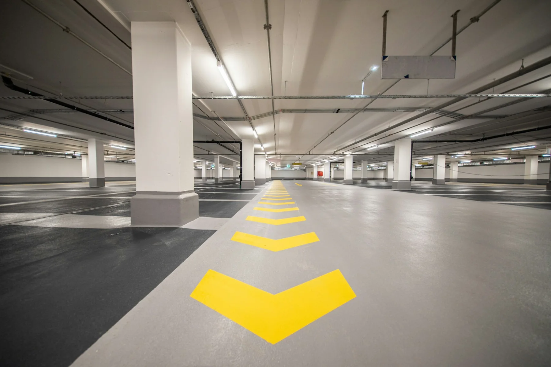 Yellow direction arrows on the floor of a bright multi-bay parking garage.