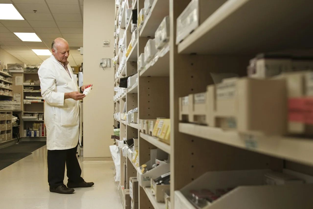 A pharmacist reviewing medication among pharmacy storage shelves.