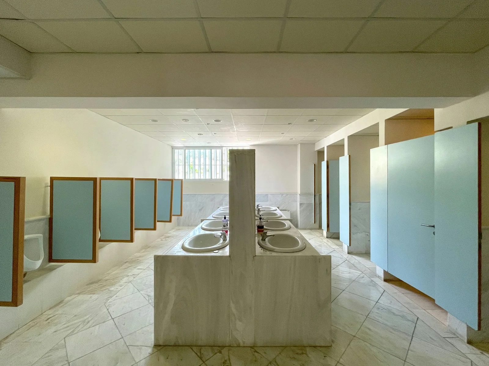 Rows of sinks and separate cubicle doors in an empty public restroom.