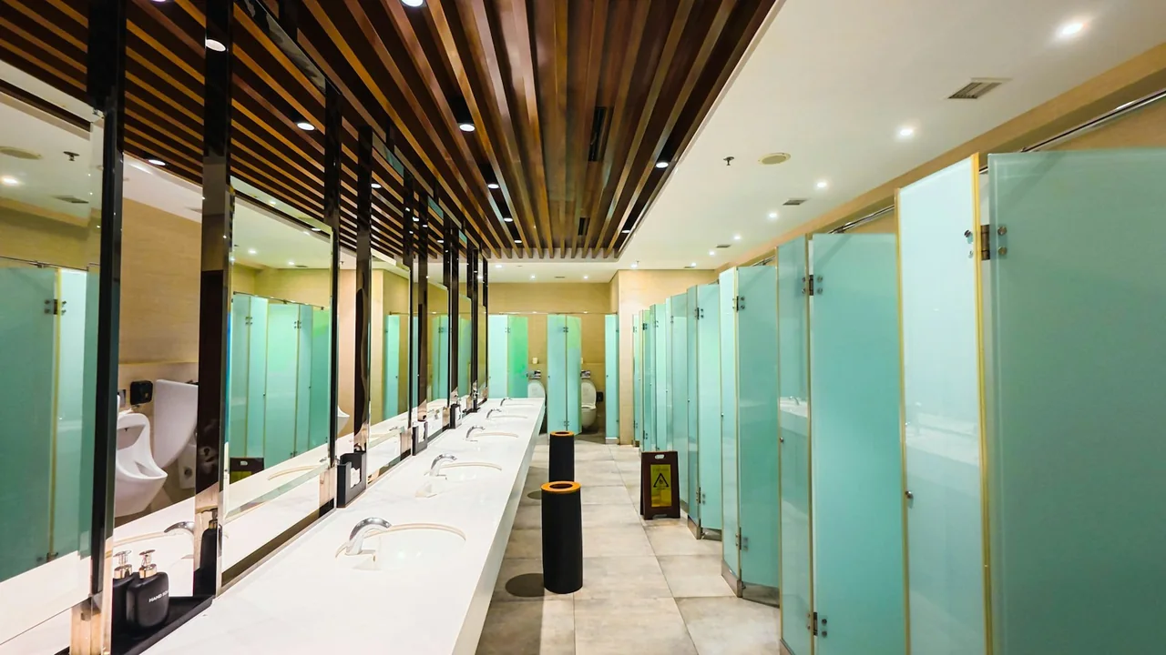 An empty public restroom with sinks and a row of closed cubicle doors.