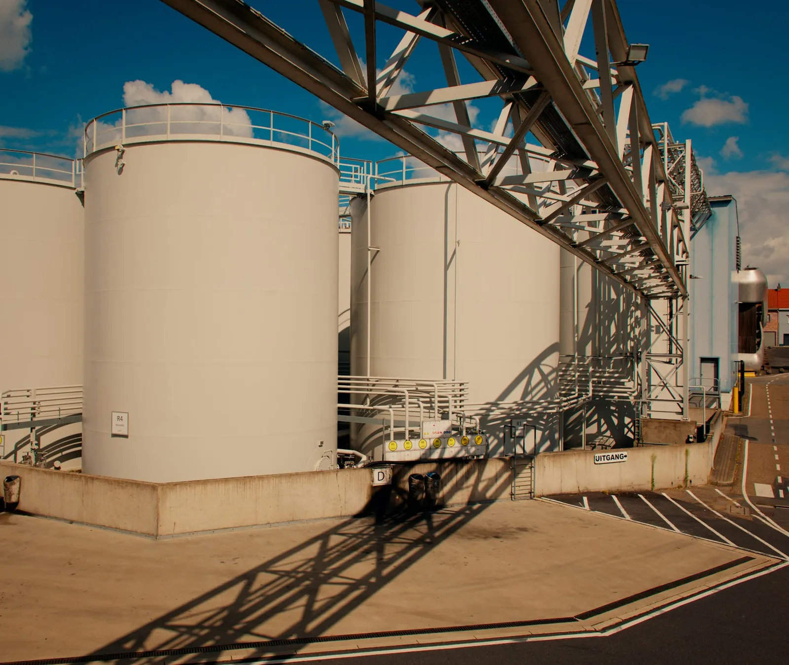 Large cylindrical industrial storage tanks beneath an overhead pipe structure.